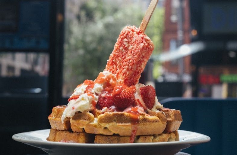 A delicious plate of strawberry shortcake waffles topped with whipped cream, fresh strawberries, and a strawberry ice cream bar at Diner 24 in Times Square, NYC